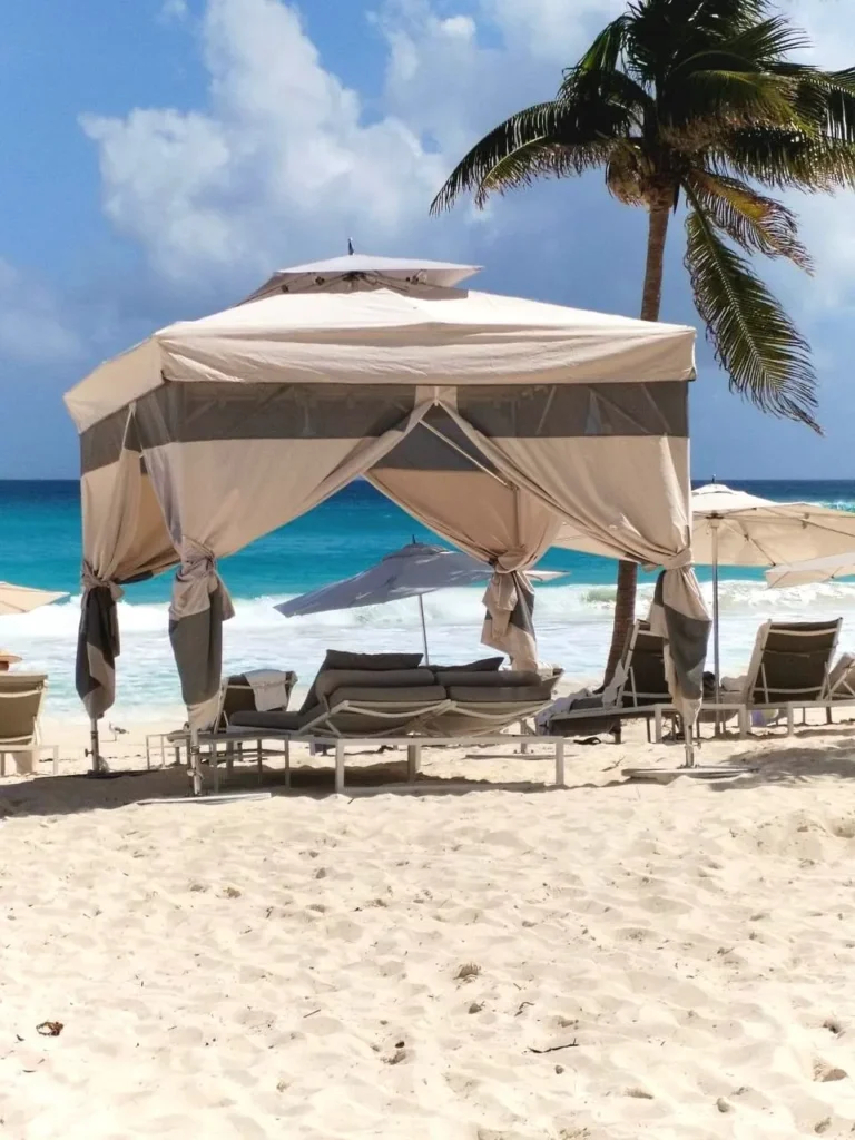 cabaña grande color beish para playa con palmeras y camastros alrededor